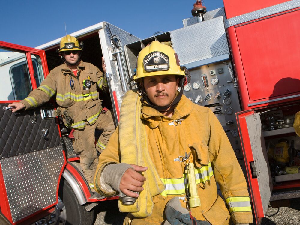 Firefighters in turnout gear beside a fire engine, served by the Public Servant Hearing Plan at AUDIO-LOGIC, PC in Columbus, NE